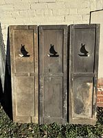 Three standing dark wooden shutters featuring sailing ship cutouts on a light background.