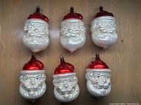 Photo showing all six vintage mercury glass Santa Claus ornaments, arranged in two rows of three on wood background, highlighting red hats and white beards.