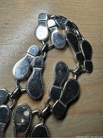 Close image showing the linked pairs of shoe sole charms forming the necklace with visible wear and texture.
