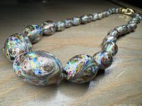 Photo focusing on the graduated large and small glass beads with multicolor swirls and metallic gold accents on a wooden surface.