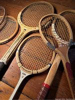 Close-up view of five wooden rackets piled on a wooden surface showing string patterns and wooden frames with decorative graphics