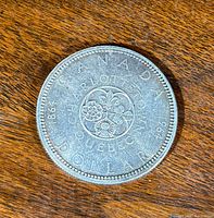 Reverse side of the 1964 Canadian silver dollar showing the Charlottetown and Quebec City emblem for Confederation anniversary, with floral symbols for French, Irish, Scottish and English heritage.