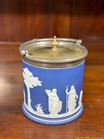 Full view of the Wedgwood Jasperware biscuit barrel showing cobalt blue body with white classical relief decoration and silver plate lid.