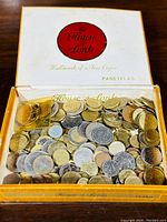 Top-down photo of the wooden House of Lords cigar box filled with various international circulated coins in different metals and sizes.