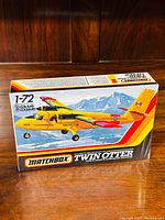 Front of box showing colorful illustration of yellow/red Twin Otter plane with mountain background, scale 1/72