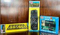 Photo showing all three items: yellow packaged metal truss bridge, figure 8 pier set in blister pack, and blue boxed automatic crossing gate.