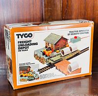 Box showing set artwork with tractor, flat car, pipe load, depot building, and remote control unit