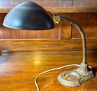 Full view of vintage adjustable gooseneck desk lamp on wooden surface showing cast iron base, silk wrapped gooseneck, and metal shade.