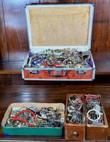 Open metal suitcase filled with mixed costume jewelry pieces