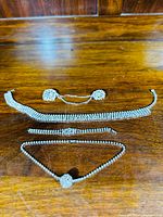 Vintage rhinestone demi-parure set displayed on wooden surface including choker necklace, bracelet, detailed necklace, and earrings with chain.