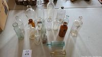 Wide shot showing assortment of 16 antique glass bottles of varying colors and shapes.
