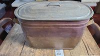 Front perspective of antique copper boiler with tin lid on rustic wooden table