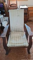 Front view of antique Morris chair showing striped upholstery on high back and seat with wooden armrests and carved legs.