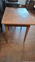 Side view of antique pine tavern table showing tabletop and tapered legs on wood floor.