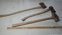 Photo showing the three tools side by side with a ruler for scale, includes two axes and one sledgehammer, all showing wear on wooden handles and metal heads.