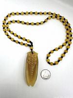 Full view of yellow jade cicada pendant necklace laid next to a quarter for scale.