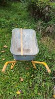Front view of the galvanized metal wheelbarrow showing interior tub and handles, placed on grass.