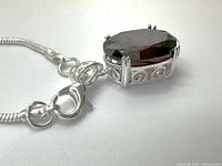 Close-up of the lobster clasp and side of the pendant showing the intricate silver scrollwork and detail of the garnet gem.