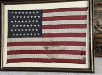 Full front view of sewn American flag with 48 stars in a gold-tone frame lying flat on carpeted surface.