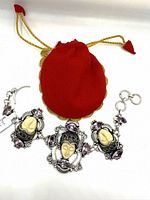 Full view of sterling silver bracelet with three white jade carved faces and amethyst stones arranged on ornate filigree links, alongside red drawstring gift pouch.