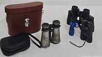 Photo showing all binoculars and two carrying cases, including vintage Century Mark IV 8x40 binoculars, antique binoculars, Fisher Investments binoculars, and others