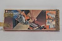 Photo of the original box packaging showing the Black & Decker Workmate work center with saw and mitre guide setup on top of the work surface.