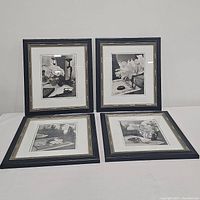 Four black framed black and white floral prints arranged on a white surface, all visible showing different images.
