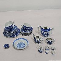 Overall assortment of the blue and white ceramic tea set items including cups, plates, teapot, creamers, and miniatures arranged on a surface