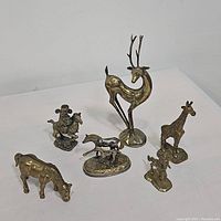 Overview photo of all six brass statues including deer, giraffe, cow, horse rider, pair of dogs, and small seated dog.