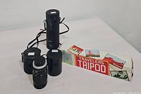 Three black camera lens cases along with boxed tripod and Canon lens on table