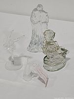 Full view of all four crystal figurines on a white surface: Waterford bride and groom, Hummel child figurine, crystal angel, and Swarovski ballerina