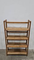 Front view of the assembled solid wood foldable bookshelf with four shelves against a white background.