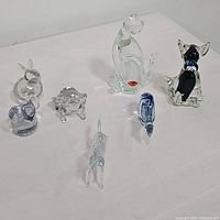 Seven glass animal figurines arranged on a white surface showing the entire lot