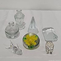 Seven glass pieces including paperweights and bottles arranged on a white surface, showing shapes and details.