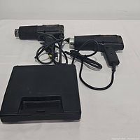 Two vintage Black & Decker Heat 'N Strip electric paint remover heat guns with cords, and a black Weller soldering kit case. Tools are placed on a white surface with cords loosely arranged.