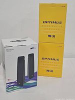 Photo of boxed Boston Acoustics MM220 computer speaker system and two boxed Optimus PRO LX5 bookshelf speakers stacked vertically.