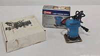 Three tools: Ryobi finishing sander in original box, blue finishing sander tool, and Dremel moto-tool.