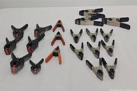 Assortment of spring clamps including black and orange plastic clamps and various metal clamps.