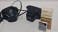 Two camera cases along with Koss AC adapter box, Nikon lens box, and Vivitar filter box on a white surface.