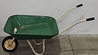 Side profile of the green basin wheelbarrow with white frame and black handle grips. Shows the basin shape, wheel and loose left arm.