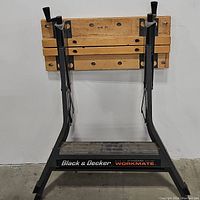 Front view of the workbench folded and standing upright showing the black metal frame and wooden top boards.