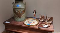 Photo showing the ceramic Uncle Sam statue, metal milk jug with eagle design, needlepoint seal wall art plate, two brass eagle bookends and wooden wall plaque all displayed on wooden furniture.