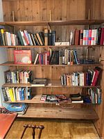 Bookshelf with various books including vintage literature, nautical guides, and fiction, arranged on wooden shelves against wood-paneled wall.