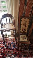 Full view of child's chair with needlepoint floral panel and wooden stool with thatched seat viewed side by side on carpet.
