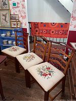 Full view of five standard wood framed dining chairs with floral embroidered cushioned seats and curved horizontal slat backs