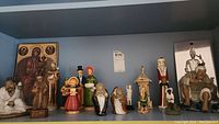 Photo of full shelf showing collection of figurines including monks, Christmas carolers, Santa, religious icon and warrior figurines