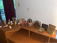 Wide view of entire lot on wooden corner desk showing figurines, bowl, turkey decoration, bookends, and pillow on a wooden desk.