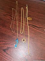 All four pieces displayed together on wood surface: plain chain, enamel fish pin, heart pendant chain, bead necklace