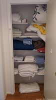 Shelf closet with multiple folded linens including blankets, sheets, and mattress covers in various colors and patterns