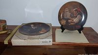 Two Norman Rockwell collectible plates displayed side by side, one on a stand and one in original box
